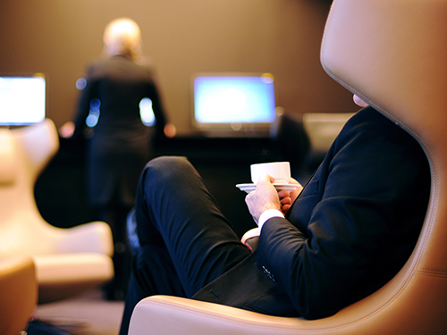 Man wearing a black suit enjoying a cup of coffee while relaxing in a chair | Coor